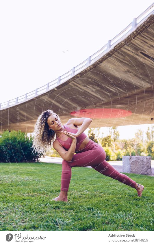 Focused woman practicing yoga in park revolved crescent lunge parivrtta anjaneyasana flexible pose twist practice balance position slim female wellness harmony