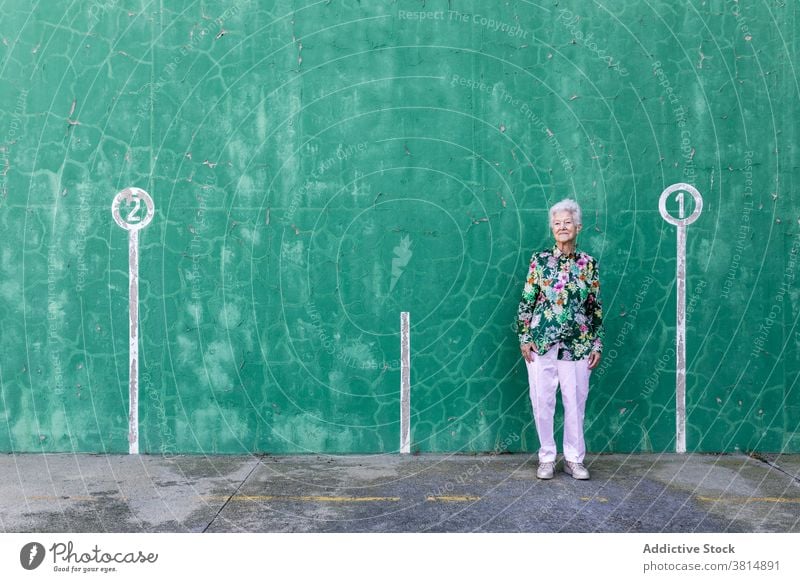Stylish senior woman standing near wall aged style elegant outfit confident positive content elderly female gray hair smile lifestyle optimist old experience