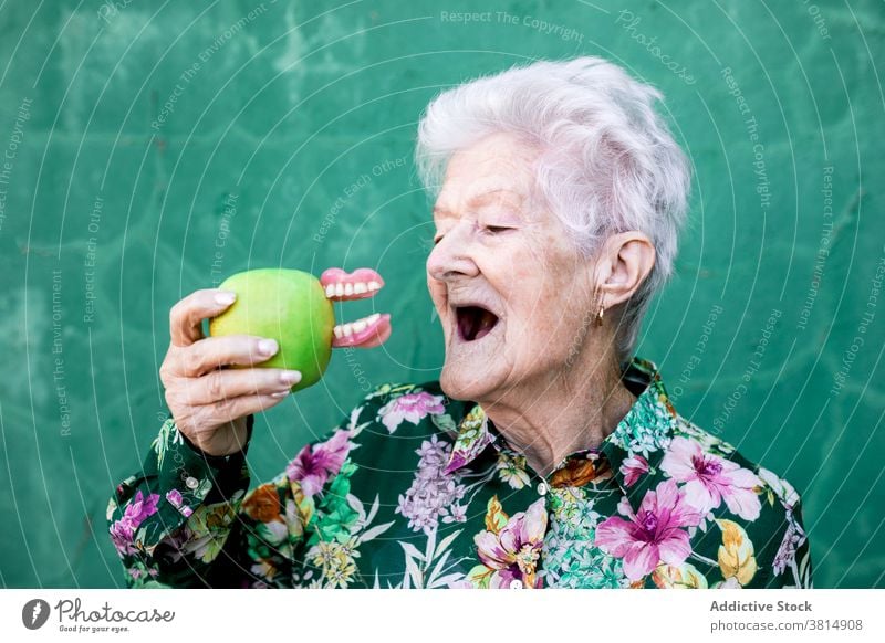 Funny senior woman with apple and denture teeth funny joke humor trendy style bite elderly female accessory lady old health care mouth aged retire dental