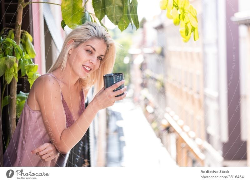 Young woman with cup of coffee enjoying morning on balcony happy drink pure smile sunny young female beverage tea relax cheerful blond lifestyle mug positive