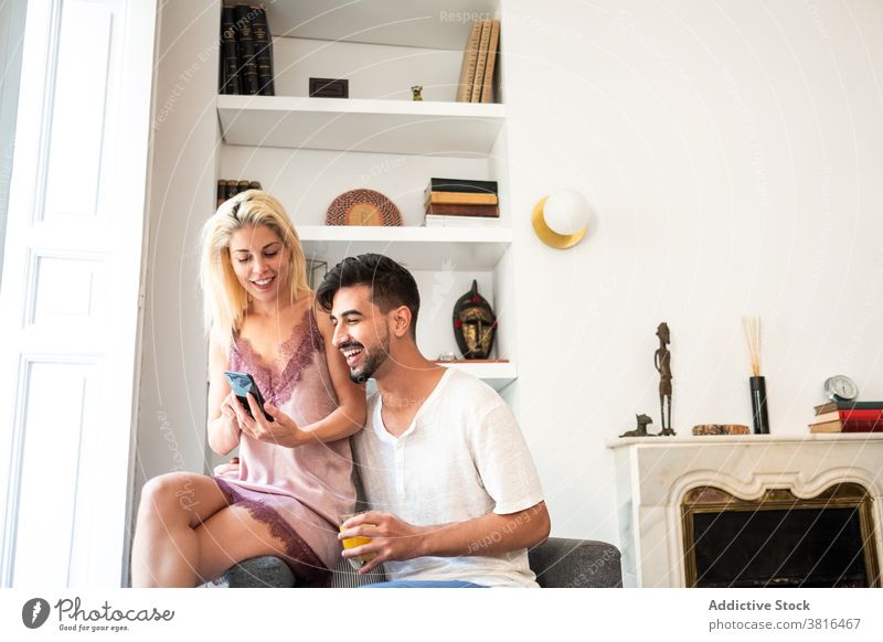 Smiling couple enjoying morning together at home early pajama sleepwear tender smartphone juice glass device gadget smile conversation relationship talk