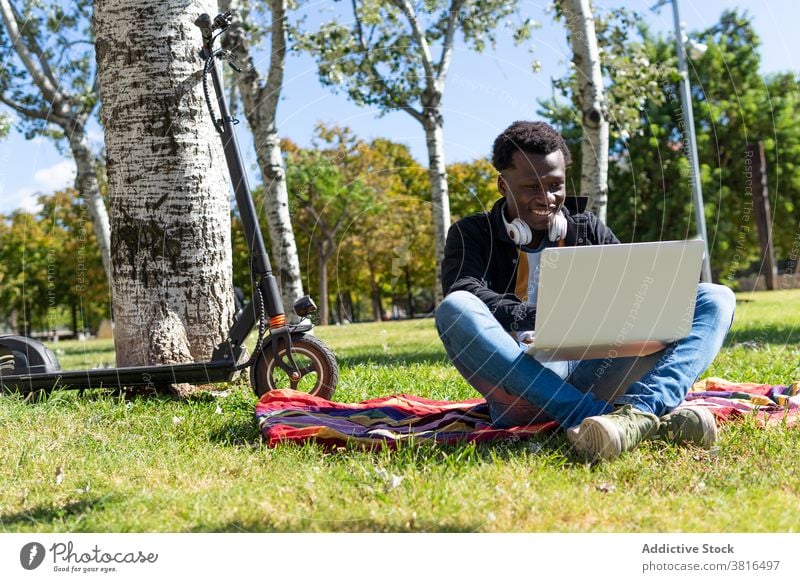 Cheerful black man working on computer in park relax laptop summer scooter hipster young device weekend male ethnic african american tree urban garden rest