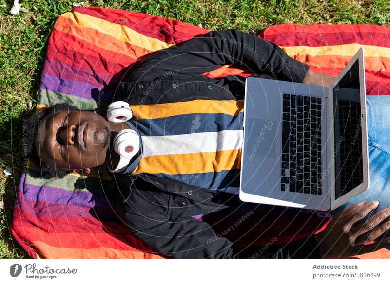 Carefree black man lying on blanket with laptop in park tired freelance sleep nap remote entrepreneur male ethnic african american netbook city work sunny