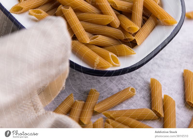 Dry pasta in bowl and on table in kitchen dry penne dried macaroni oil olive bottle arrangement italian food metal napkin meal composition organic cuisine