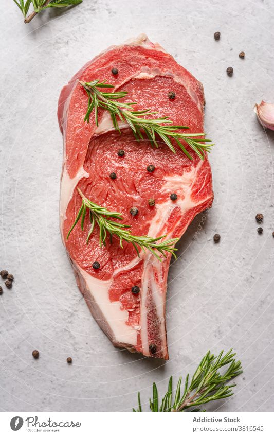 Raw beef steak with herbs on table raw bone t bone rosemary garnish meat pepper black kitchen cook food cuisine delicious dish spice gourmet fresh recipe sprig