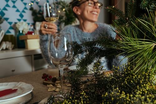 family chatting at christmas dinner, two sisters sitting at the decorated table with glasses of white wine in hand. thanksgiving women smile together talk