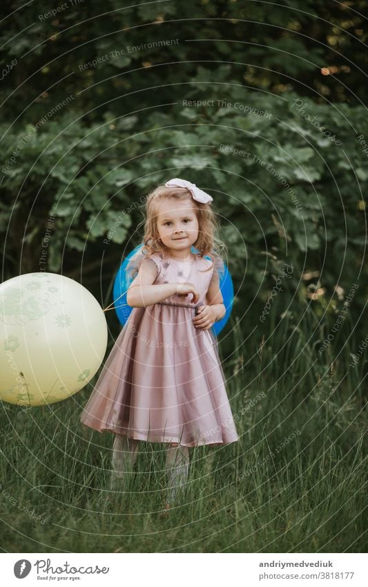 Stylish baby girl 4-5 year old holding big balloon wearing trendy pink dress in meadow. Playful. little girl with a balloon in the park. Birthday party. child