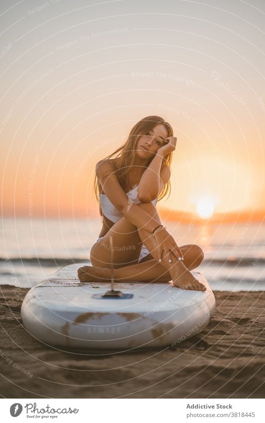 Carefree woman on paddleboard in sea relax sunset sup sand surfboard slim sundown female swimsuit ocean summer sit rest beach enjoy holiday nature fit sky