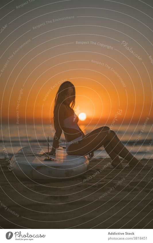 Slim woman on paddle board on beach paddleboard sup sand sunset sit relax sea female swimsuit fit slim summer coast sky nature enjoy surfboard lady slender rest