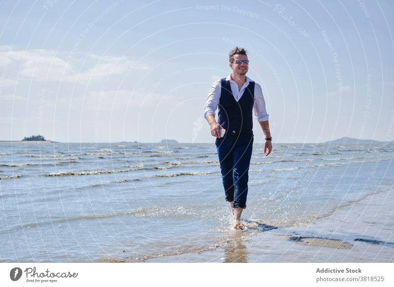Cheerful businessman in suit having fun on wavy ocean stylish outfit carefree blue sky cloudy water apparel barefoot sea ripple horizon cheerful formal wear