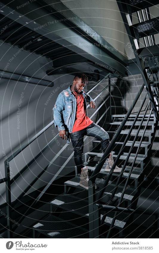 Black man in stylish clothes on metal stairs trendy apparel denim jacket street style fashion thoughtful appearance male ethnic black african american staircase