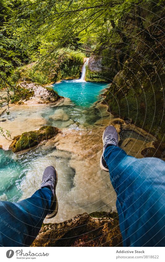 Faceless traveler enjoying cascade and pond from mountain tourist admire nature highland flow vegetate bright contemplate sneakers jeans tree environment ripple