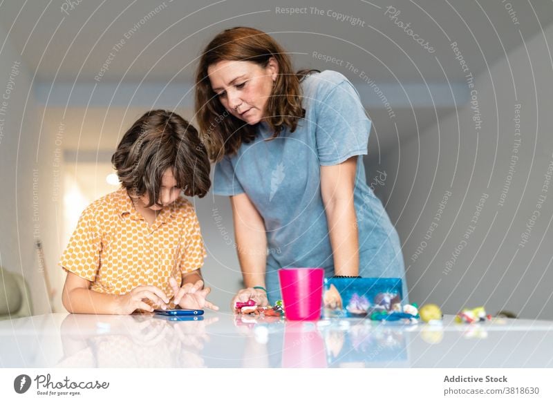 Mother and anonymous son chatting on smartphone at home mother internet childcare motherhood spend time childhood toy using gadget surfing woman boy spare time