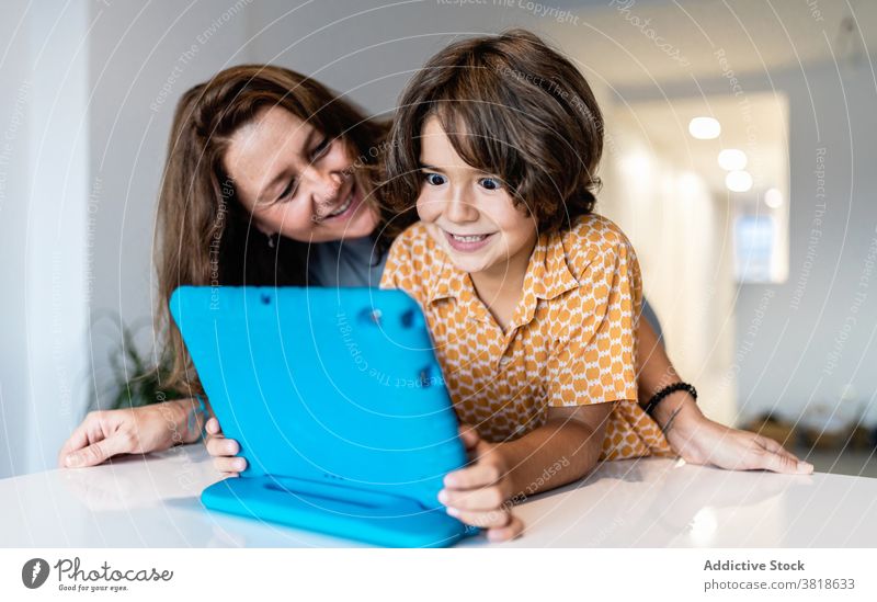 Excited boy with laptop near smiling mother at home excited childhood motherhood spare time weekend using gadget cheerful woman watching internet online table