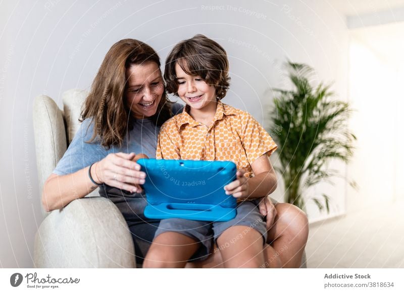Excited boy with laptop with smiling mother at home sit couch excited childhood browsing motherhood spare time weekend using gadget cheerful woman watching