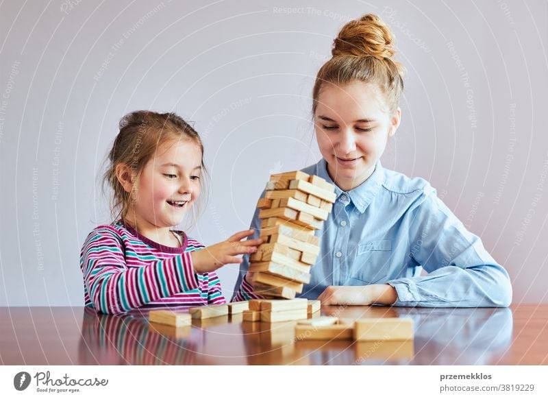 Little girl preschooler and her elder sister playing together with wooden blocks game toy activity brick build child childhood concept construction copy space