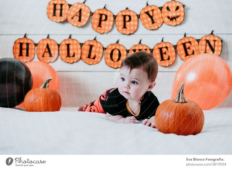 cute baby girl in halloween costume at home, sitting on bed with Halloween decoration, Lifestyle indoor indoors trick or treat pumpkin balloons orange october