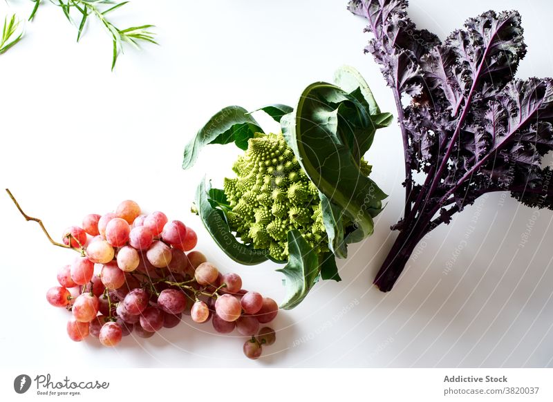Flatlay with purple kale, pink grapes and romanesco cabbage food fruit vegetable herb assorted produce vegetarian flat lay top view white cutting board various