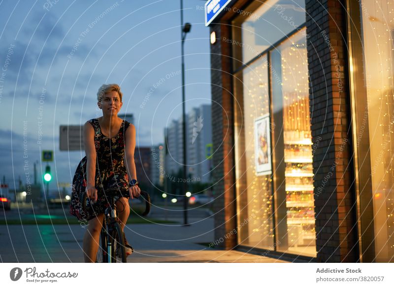 Woman in dress rides bicycle in night city bike evening walk girl young riding beautiful lights building glass window showcase store posing attractive trip