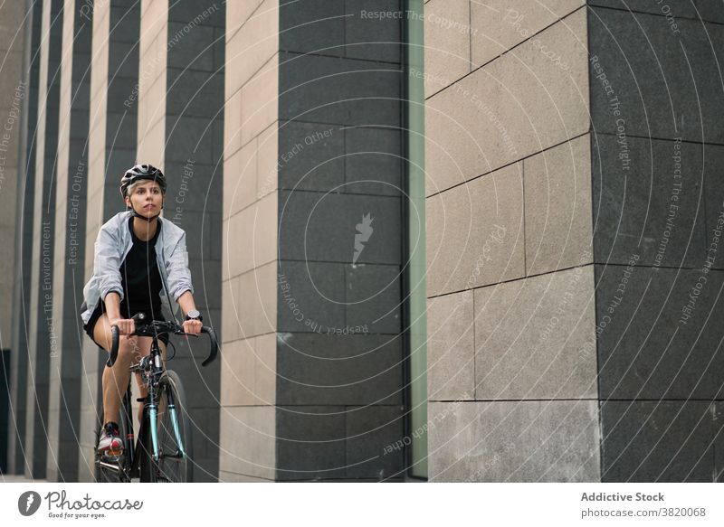 Female courier cycling near tall building in city on summer day Cyclist bricked woman young sports riding helmet protective girl delivery entertainment