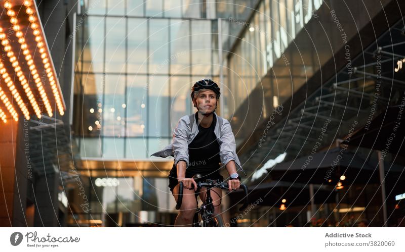 Female courier cycling near tall building with glass windows in city Cyclist bricked day woman young sports riding summer helmet protective girl delivery