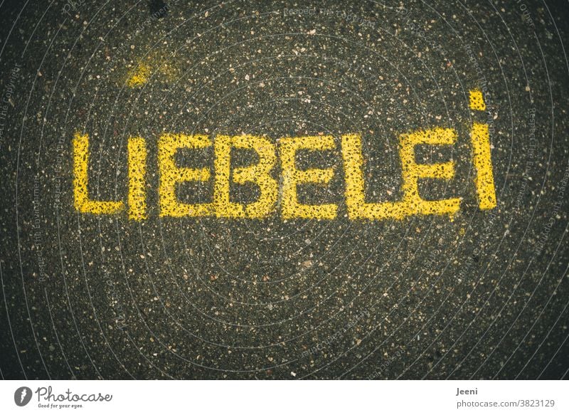 A path with street painting with the word "LIEBELEI" | text on a monochrome neutral background Love Dating Street painting off Asphalt