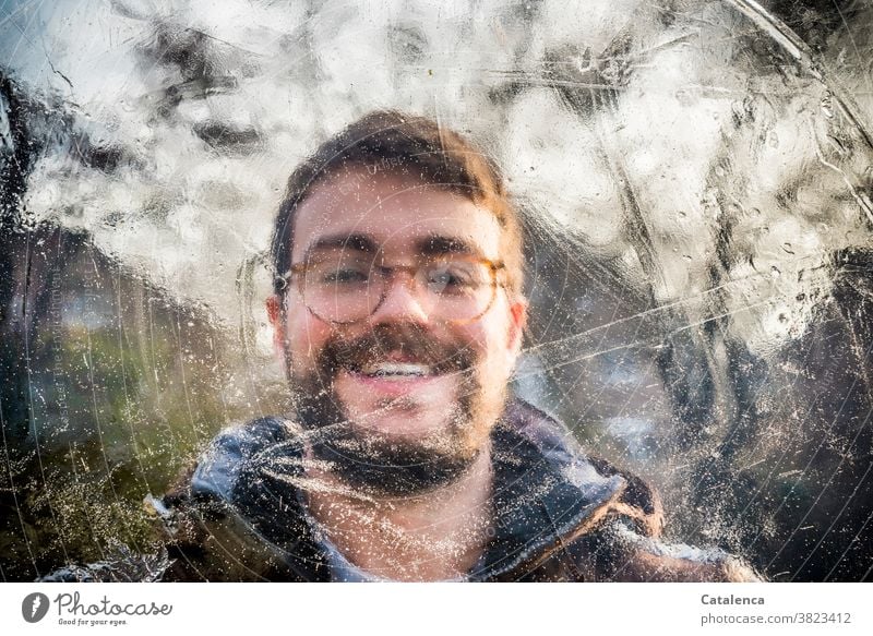 Portrait of a smiling young man behind ice Young man smilingly Facial hair Eyeglasses Brunette person masculine Winter Ice Frozen Cold Brown Green Day daylight