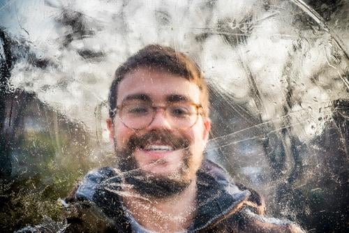 Portrait of a smiling young man behind ice Young man smilingly Facial hair Eyeglasses Brunette person masculine Winter Ice Frozen Cold Brown Green Day daylight