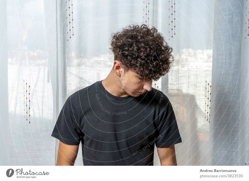 Attractive young man with curly hair wearing black t-shirt posing on white curtains background cheerful casual smile male adult handsome happy attractive