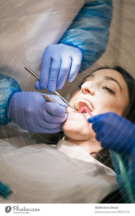 Unrecognizable dentist examining teeth of patient in clinic stomatology examine process oral procedure tool uniform nurse using medical equipment health care