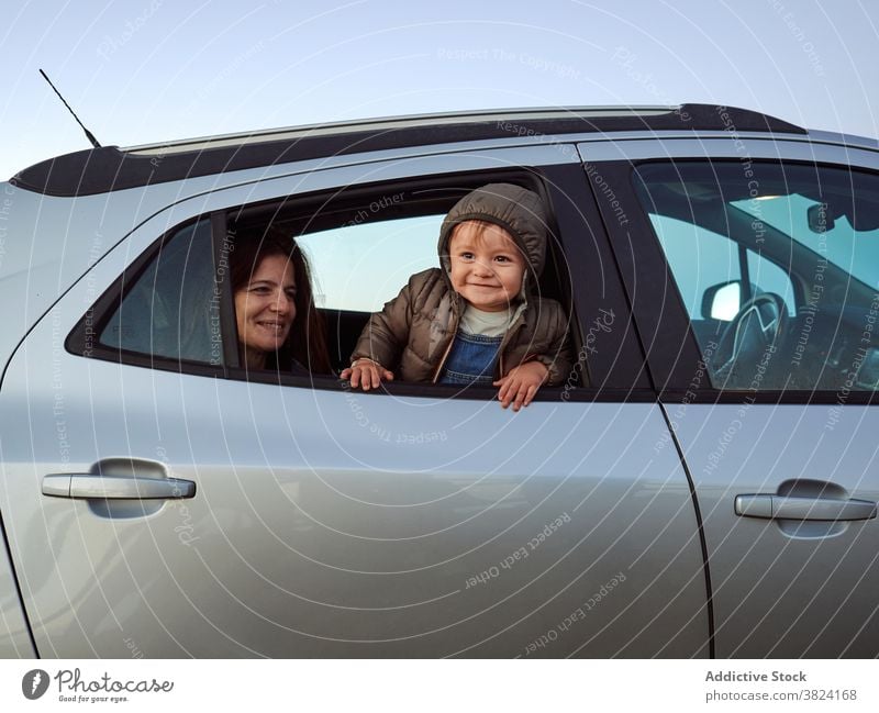 Mother and child together in car peer window curious mother automobile backseat toddler cute cheerful transport vehicle kid little smile travel rest childhood