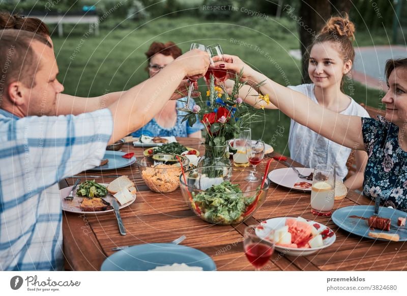 Family making toast during summer picnic outdoor dinner in a home garden feast having food man together woman child barbecue table eating gathering people