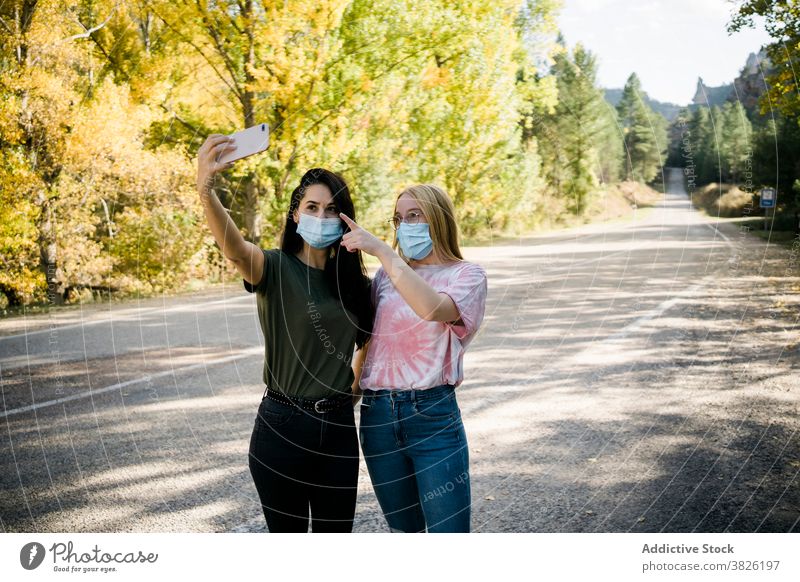 Young women in medical masks taking selfie in countryside friend coronavirus road forest smartphone happy friendship mobile take photo share photography autumn