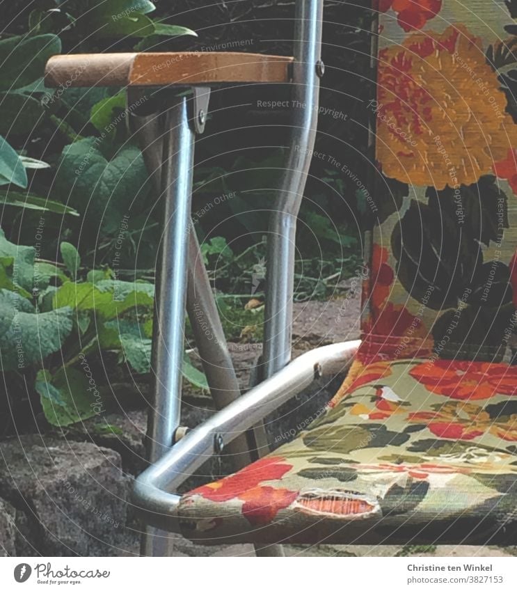 The old camping chair with the flower pattern in yellow, orange and green had seen better times. Camping chair Old still holds Flowery pattern Retro