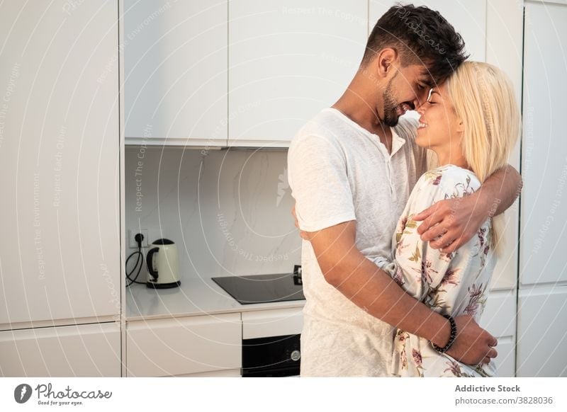 Cheerful couple hugging tenderly in kitchen embrace touch nose love together morning home domestic girlfriend boyfriend modern relationship fondness close