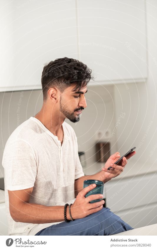 Serious man having breakfast in kitchen morning coffee smartphone early home browsing cup male domestic outfit drink gadget device calm relax modern rest online