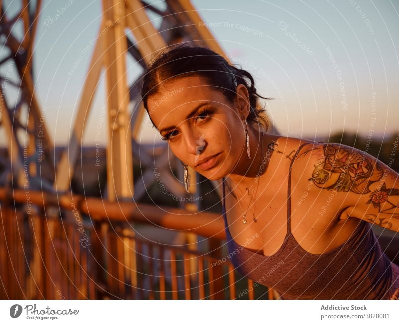 Stylish woman in tattoos standing in city style trendy bridge metal sunset summer relax rest enjoy young urban freedom delight glad evening twilight cool