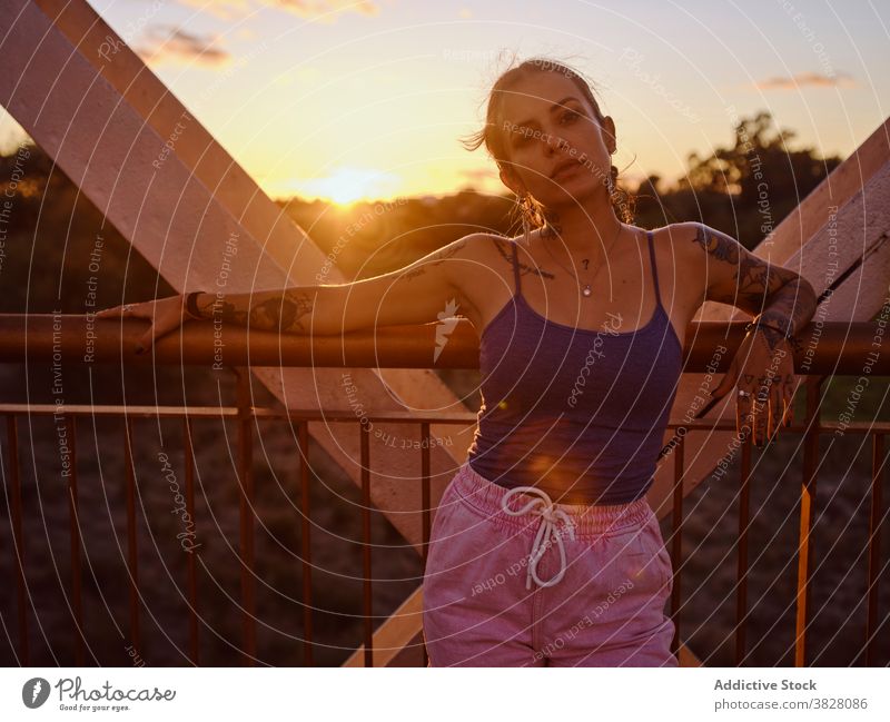 Stylish woman in tattoos standing in city style trendy bridge metal sunset summer relax rest enjoy young urban freedom delight glad evening twilight cool