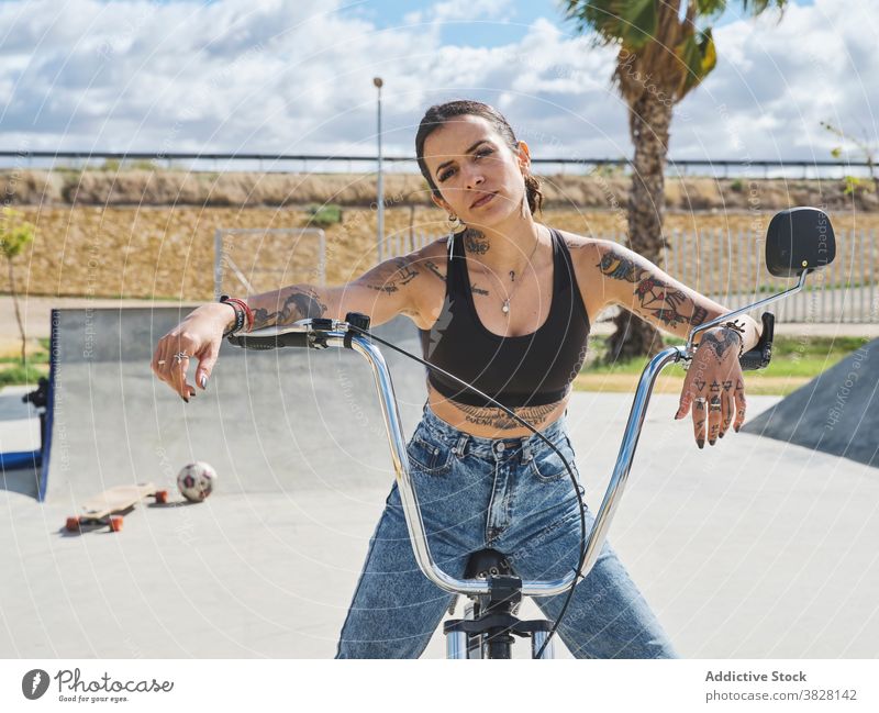 Serious woman on bike in skate park bmx confident bicycle extreme serious tattoo style female outfit sit trendy urban young cool transport freedom summer city