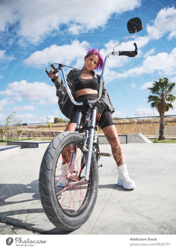 Serious woman on bike in skate park bmx confident bicycle extreme serious tattoo style female outfit sit trendy urban young cool transport freedom summer city