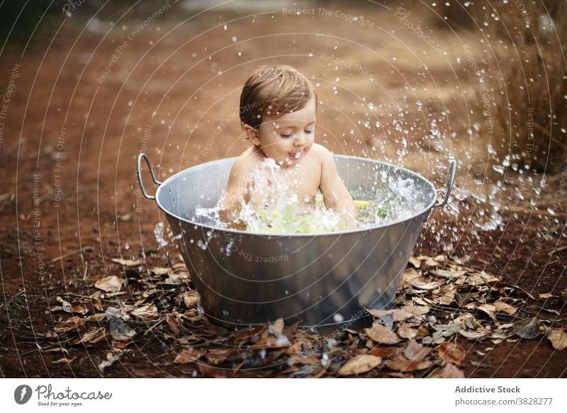 Adorable baby playing with splashing water in bath outdoors childhood having fun carefree eyes closed motion drop toddler enjoy charming fluid content innocent