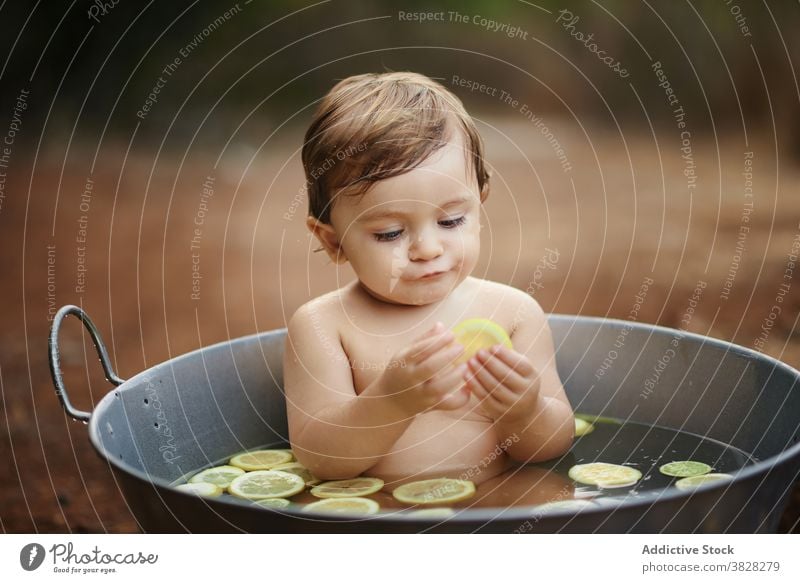 Adorable toddler child eating lemons in metal bath childhood enjoy naked charming innocent baby birthday celebrate sand land citrus fruit slice ripe fresh