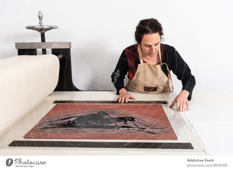 Printmaker arranging linoleum sheet with inked pattern in press printmaking linocut create craft artisan professional craftswoman artwork arrange tool master