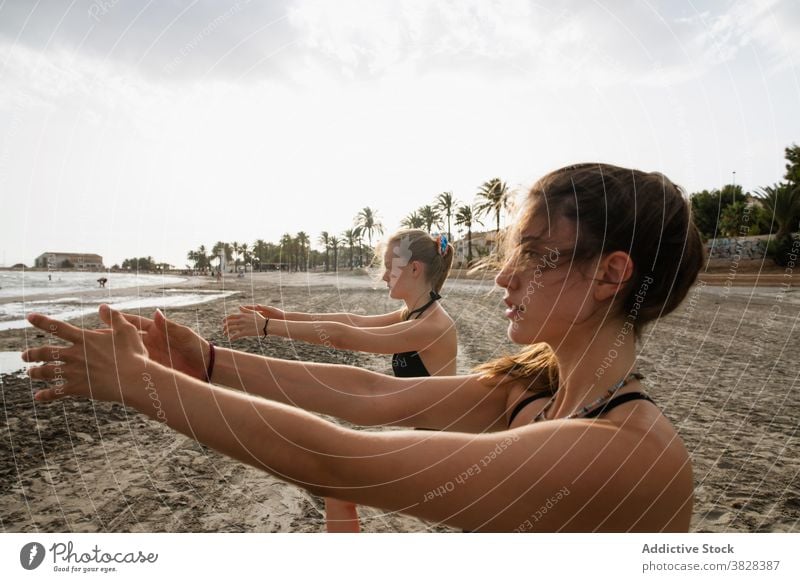 Focused friends practicing yoga in fresh air of sea women practice beach calm mindfulness stretch sandy coast outstretch focus palm cloudy day nasty gloomy