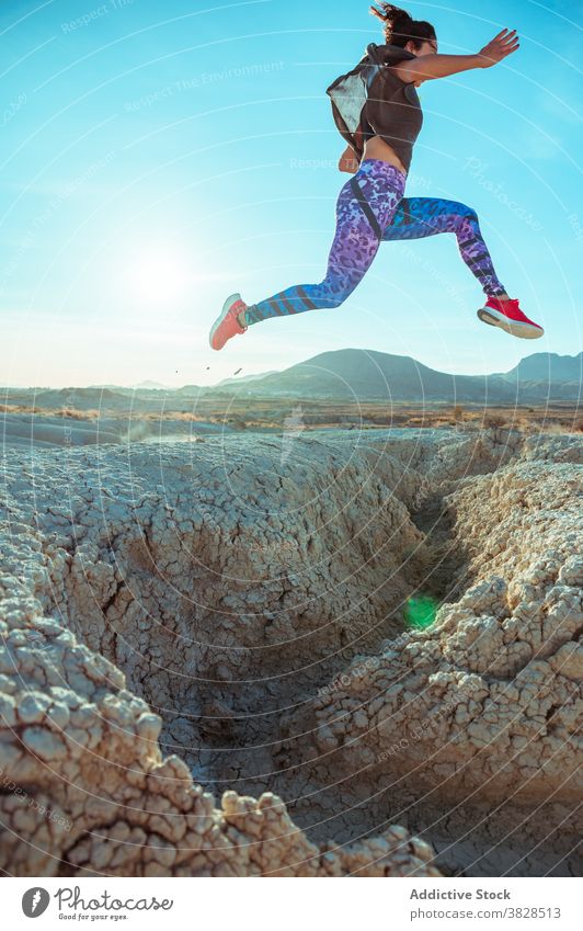 Strong sportswoman jumping over sandy hill fly skyline blue sky desert rough active energy leap athlete slope terrain nature workout training exercise female