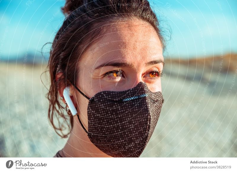 Sporty woman in mask and earphones standing among dry terrain sportswoman earbuds desert confident listen protect wireless strong determine coronavirus covid 19