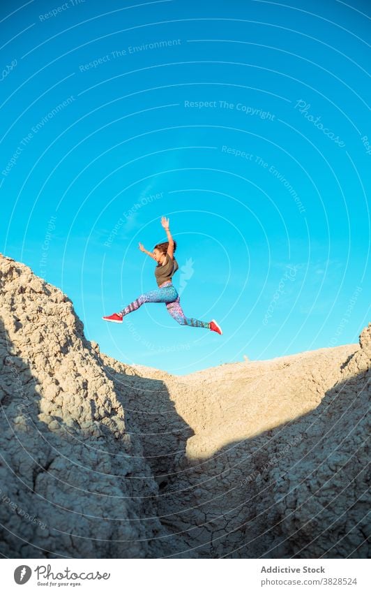 Strong sportswoman jumping over sandy hill fly skyline blue sky desert rough active energy leap athlete slope terrain nature workout training exercise female