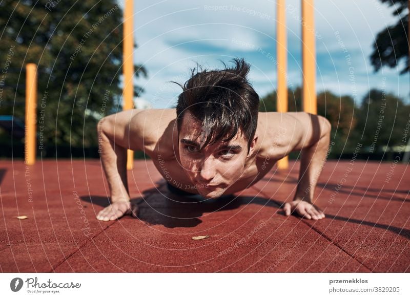 Young shirtless man bodybuilder doing push-ups on a red rubber ground during his workout in a modern calisthenics park care caucasian health lifestyle male one