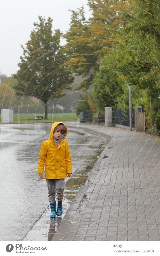 Rain walk - boy in yellow rain jacket and rubber boots walks through puddles at the roadside Human being Child Boy (child) Puddle Rain jacket Rubber boots