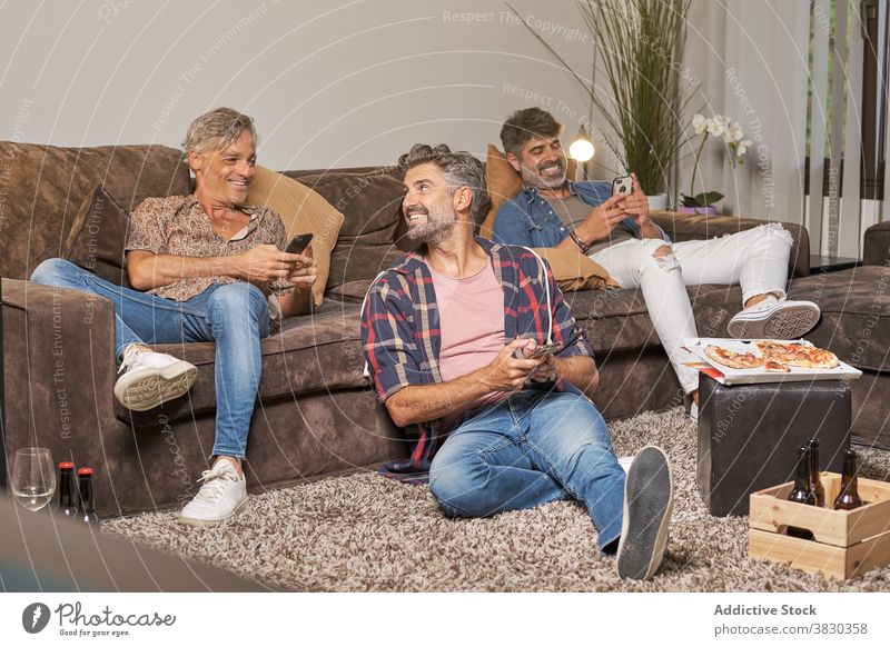 Happy friends browsing smartphones while having pizza party men cheerful leisure lounge free time chill living room fun toothy smile together alcohol friendship